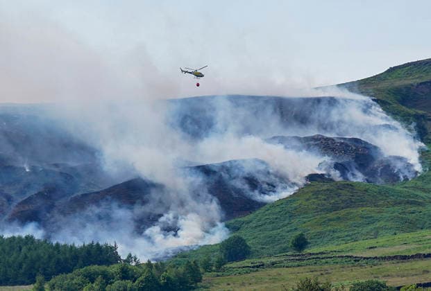 June 25, 2026, Glossop, Derbyshire, UK: Glossop, UK. A helicopter flies above a wildfire as burns near a forest in Glossop near Wood Head Reservoir, Derbyshire. A four-day amber heat and extreme heat warning has been put in place by the Met Office, with temperatures expected to peak by the end of the week. Glossop UK  - ZUMAl94_ 20260625_zaf_l94_049 Copyright: xIoannisxAlexopoulosx