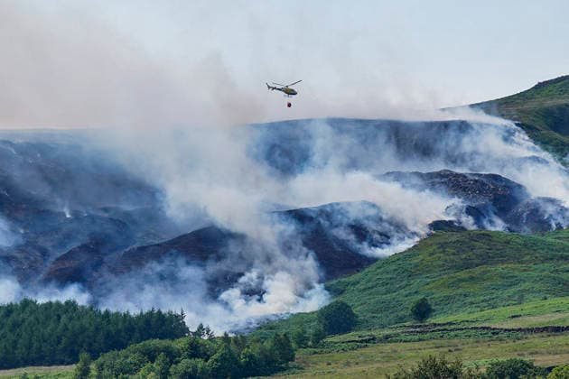 June 25, 2026, Glossop, Derbyshire, UK: Glossop, UK. A helicopter flies above a wildfire as burns near a forest in Glossop near Wood Head Reservoir, Derbyshire. A four-day amber heat and extreme heat warning has been put in place by the Met Office, with temperatures expected to peak by the end of the week. Glossop UK  - ZUMAl94_ 20260625_zaf_l94_051 Copyright: xIoannisxAlexopoulosx