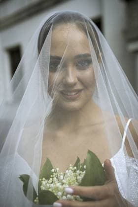 Nahaufnahme der Braut in einem weißen schulterfreien Kleid mit Schleier und einem Strauß Maiglöckchen. Die Brünette hat eine glatte Frisur, die zu einem Brötchen gebunden ist. Die Braut ist glücklich und lächelt Close-up of the bride in a white off-the-shoulder dress, with a veil, a bouquet of lilies of the valley. the brunette has a smooth hairdo tied in a bun. the bride is happy and smiling Copyright: imageBROKER HannaxNikulnikova ibxiqx18087120.jpg ,model released, Symbolfoto ,property released
