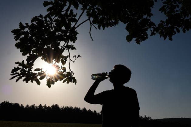 Sommer im Siegerland. Es ist sehr heiss (heiß) und die Temperaturen sollen weiter ansteigen. Der Himmel ist blau und die Sonne strahlt vom wolkenlosen Himmel. Im Vordergrund trinkt eine Frau unter einem Baum am Morgen Wasser aus einer Flasche. Sommer am 26.06.2026 in Siegen Deutschland. *** Summer in the Siegerland. It is very hot, and temperatures are expected to rise further. The sky is blue, and the sun is shining from a cloudless sky. In the foreground, a woman is drinking water from a bottle under a tree in the morning. Summer on June 26, 2026, in Siegen, Germany.