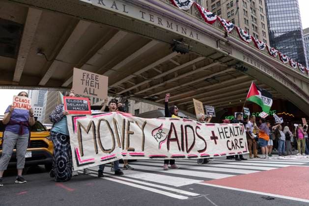 June 26, 2026, New York, New York, USA: Members of ACT UP New York begin Pride weekend with an act of civil disobedience blockading traffic during the morning rush hour on 42nd Street outside Grand Central Station stating solidarity with striking Delaney Hall immigrant detainees and denouncing Trump administration cuts to AIDS funding and healthcare. After traffic is at a standstill for approximately 40 minutes, NYPD arrests demonstrators. The protest banner is Ã¢â‚¬ËœMoney for AIDS and Healthcare Not for ICE and Warfare. Protesters hold signs that read FREE THEM ALL CLOSE DELANEY HALL. Demonstrators defend New YorkÃ¢â‚¬â ¢s sanctuary city status as an ICE surge is promised and protest funding cuts to AIDS Drug Assistance Programs (ADA - ZUMAr174 20260626_znp_r174_012 Copyright: xGinaxMxRandazzox
