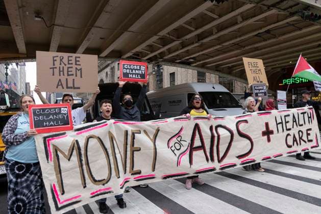 June 26, 2026, New York, New York, USA: Members of ACT UP New York begin Pride weekend with an act of civil disobedience blockading traffic during the morning rush hour on 42nd Street outside Grand Central Station stating solidarity with striking Delaney Hall immigrant detainees and denouncing Trump administration cuts to AIDS funding and healthcare. After traffic is at a standstill for approximately 40 minutes, NYPD arrests demonstrators. The protest banner is Ã¢â‚¬ËœMoney for AIDS and Healthcare Not for ICE and Warfare. Protesters hold signs that read FREE THEM ALL CLOSE DELANEY HALL. Demonstrators defend New YorkÃ¢â‚¬â ¢s sanctuary city status as an ICE surge is promised and protest funding cuts to AIDS Drug Assistance Programs (ADA - ZUMAr174 20260626_znp_r174_013 Copyright: xGinaxMxRandazzox