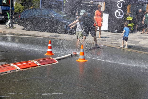 14. Landestag der Verkehrssicherheit, Nürnberg, 27.06.2026 Über einen geöffneten Feuerwehrschlauch auf der Fahrbahn versprüht Wasser auf Passanten. Die Berufsfeuerwehr Nürnberg sorgt am Jakobsplatz für Abkühlung bei sommerlichen Temperaturen. Nürnberg Bayern Deutschland *** 14th State Road Safety Day, Nuremberg, June 27, 2026 Water sprays onto passersby from an open fire hose on the road The Nuremberg Fire Department provides relief from the summer heat at Jakobsplatz Nuremberg, Bavaria, Germany 20260627-286A0397-M4000