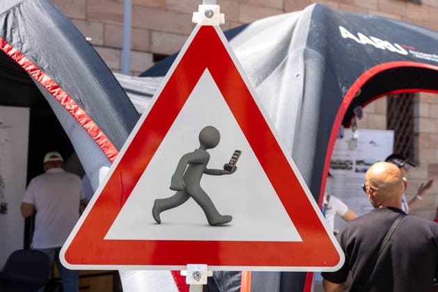 14. Landestag der Verkehrssicherheit, Nürnberg, 27.06.2026 Warnschild mit einer Piktogramm-Figur, die beim Laufen ein Smartphone nutzt. Das Schild thematisiert die Ablenkungsgefahr durch Mobiltelefone im Strassenverkehr. Nürnberg Bayern Deutschland *** 14th State Road Safety Day, Nuremberg, June 27, 2026 Warning sign featuring a pictogram of a person using a smartphone while walking. The sign highlights the danger of distraction caused by cell phones in traffic. Nuremberg, Bavaria, Germany 20260627-286A0406-M4000