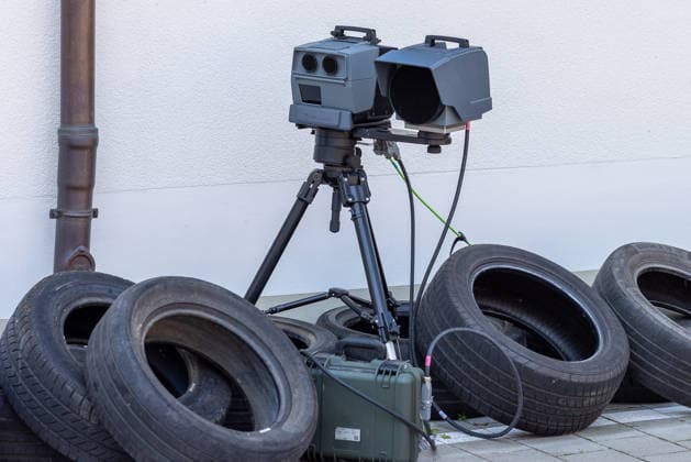14. Landestag der Verkehrssicherheit, Nürnberg, 27.06.2026 Eine stationaere Geschwindigkeitsmessanlage (Laserscanner mit Kameraeinheit) steht auf einem Stativ vor einer Wand, umgeben von alten Autoreifen. Ein olivgruener Transportkoffer liegt darunter. Das Geraet ist verkabelt und betriebsbereit aufgebaut. Nürnberg Bayern Deutschland *** 14th State Road Safety Day, Nuremberg, June 27, 2026 A stationary speed measurement system—a laser scanner with a camera unit—stands on a tripod in front of a wall, surrounded by old car tires. An olive-green carrying case lies beneath it. The device is wired up and set up and ready for operation. Nuremberg, Bavaria, Germany 20260627-286A0450-M4000