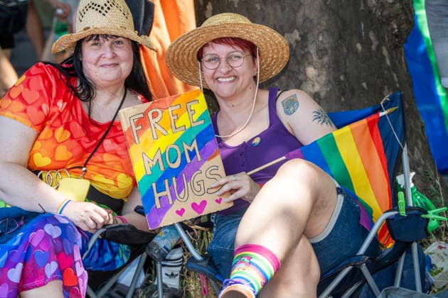 Ausgelassene Stimmung, auch bei den Zuschauern, wie hieran der Sonnenstraße, zwei Frauen bieten Free Mom Hugs an, sitzen mit Regenbogenfahnen am Rande der Strecke, CSD 2026, große Politparade, Höhepunkt der Pride Weeks, München, 27. Juni 2026 Deutschland, München, 27. Juni 2026, ausgelassene Stimmung, auch bei den Zuschauern, wie hieran der Sonnenstraße, zwei Frauen bieten Free Mom Hugs an, kostenlose Umarmungen, sitzen im Schatten mit Regenbogenfahnen am Rande der Strecke, CSD 2026, große PolitParade mit Hunderttausenden Zuschauern und Teilnehmern, im Rahmen der Pride Weeks, Motto Unsere Vielfalt. Unsere Stärke., Christopher Street Day, größte Demonstration von Lesben, Schwulen, Bisexuellen, trans*, inter* und queeren Menschen (L