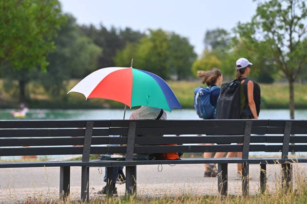 Wetterbild vom 28.06.2026. Ein Mann sitzt auf einer Bak im Riemer Park in Muenchen Messestadt Riem und sucht Schatten unter einem Regenschirm, der als Sonnenschirm fungiert, *** Weather photo from June 28, 2026: A man sits on a bench in Riemer Park in Munich s Messestadt Riem neighborhood, seeking shade under an umbrella that is being used as a parasol,