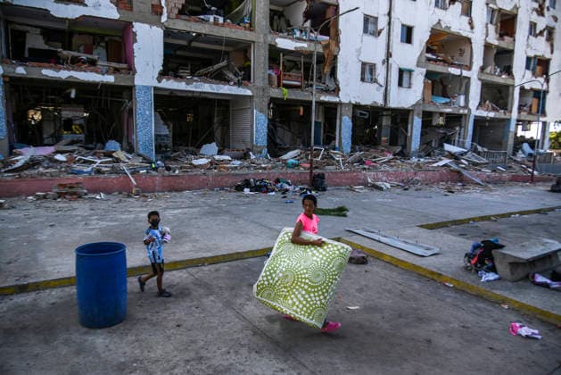 A Venezuelan woman walks carrying her belongings past destroyed buildings as rescue teams continue searching for victims amid debris of a demolished building after a magnitude 7.2 earthquake struck Venezuela and other regions in the Caribbean in La Guaira, Venezuela, on June 27, 2026. According to the U.S. Geological Survey, a powerful 7.5?magnitude aftershock struck after the main quake. Medical and media sources reported that the death toll has risen to around 1,500, with some 3,000 others injured. A web page created to track the missing has listed nearly 50,000 people as unaccounted for. photo by Jonathan Lanza  VAN2026062812 JonathanxLanza