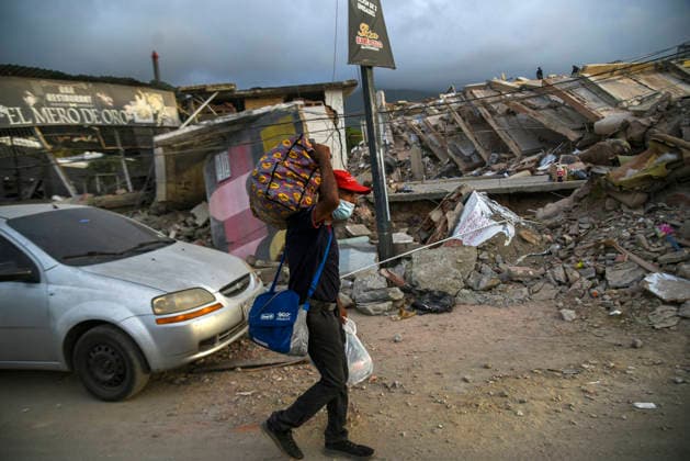 A Venezuelan man walks carrying his belongings past destroyed buildings as rescue teams continue searching for victims amid debris of a demolished building after a magnitude 7.2 earthquake struck Venezuela and other regions in the Caribbean in La Guaira, Venezuela, on June 27, 2026. According to the U.S. Geological Survey, a powerful 7.5?magnitude aftershock struck after the main quake. Medical and media sources reported that the death toll has risen to around 1,500, with some 3,000 others injured. A web page created to track the missing has listed nearly 50,000 people as unaccounted for.  VAN2026062817 JonathanxLanza