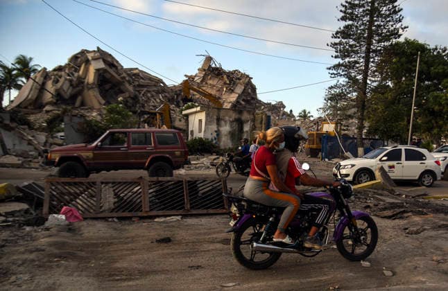 Venezuelans ride motorcycles past destroyed buildings as rescue teams continue searching for victims amid debris of a demolished building after a magnitude 7.2 earthquake struck Venezuela and other regions in the Caribbean in La Guaira, Venezuela, on June 27, 2026. According to the U.S. Geological Survey, a powerful 7.5?magnitude aftershock struck after the main quake. Medical and media sources reported that the death toll has risen to around 1,500, with some 3,000 others injured. A web page created to track the missing has listed nearly 50,000 people as unaccounted for.  VAN2026062821 JonathanxLanza
