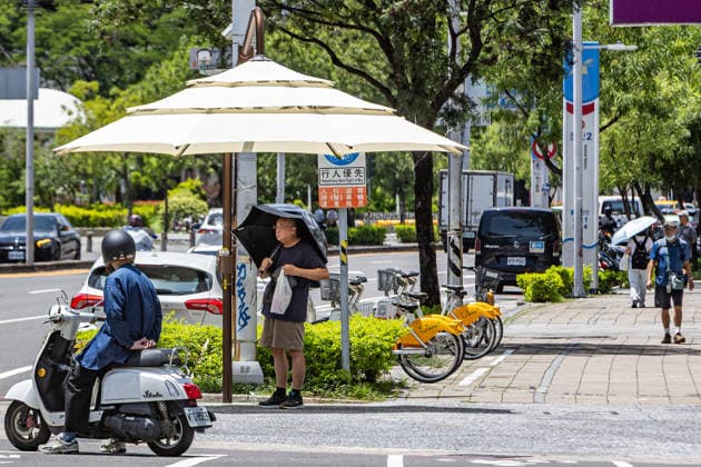 July 1, 2026, Kaohsiung City, Kaohsiung City, Taiwan: A scooter rider stops near a resident standing under Kaohsiung s newly trialed manual public parasol alongside a row of docked shared bicycles on July 1, 2026 Kaohsiung City Taiwan - ZUMAh198 20260701_zip_h198_007 Copyright: xCheng-ChiaxHuangx