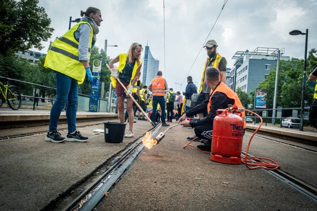 Leipziger Bürgerinnen und Bürger befreien am Johannisplatz gemeinsam mit den Leipziger Verkehrsbetrieben (LVB) die Straßenbahngleise von geschmolzenem Bitumen. Nachdem bereits am Vortag rund 100 Freiwillige einem Aufruf der LVB gefolgt waren, wurden die Reinigungsarbeiten am zweiten Tag am Johannisplatz fortgesetzt. Hintergrund sind die Schäden durch die extremen Temperaturen des vergangenen Hitzewochenendes. Aufnahme vom Datum . Reinigung Leipzig *** Residents of Leipzig, together with the Leipzig Public Transportation Authority (LVB), are clearing melted asphalt from the tram tracks at Johannisplatz. After about 100 volunteers had already responded to a call for help from the LVB the previous day, cleanup efforts continued on the sec