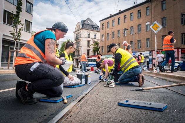 Freiwillige Helfer reinigen gemeinsam mit Mitarbeitenden der Leipziger Verkehrsbetriebe (LVB) Straßenbahngleise an der Leibnizstraße in Leipzig (Sachsen) von geschmolzenem Bitumen. Die Arbeiten sind Teil eines dritten Subbotniks zur Beseitigung der Hitzeschäden am Straßenbahnnetz. Aufnahme vom 4. Juli 2026. Hilfsaktion Leipzig *** Volunteers are working alongside employees of the Leipzig Public Transportation Authority (LVB) to clean melted bitumen from the tram tracks on Leibnizstraße in Leipzig, Saxony. The work is part of a third subbotnik aimed at repairing heat damage to the tram network. Photo taken on July 4, 2026. VolunteerLeipzig Relief Effort