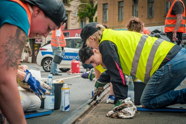 Freiwillige Helfer reinigen gemeinsam mit Mitarbeitenden der Leipziger Verkehrsbetriebe (LVB) Straßenbahngleise an der Leibnizstraße in Leipzig (Sachsen) von geschmolzenem Bitumen. Die Arbeiten sind Teil eines dritten Subbotniks zur Beseitigung der Hitzeschäden am Straßenbahnnetz. Aufnahme vom 4. Juli 2026. Hilfsaktion Leipzig *** Volunteers are working alongside employees of the Leipzig Public Transportation Authority (LVB) to clean melted bitumen from the tram tracks on Leibnizstraße in Leipzig, Saxony. The work is part of a third subbotnik aimed at repairing heat damage to the tram network. Photo taken on July 4, 2026. VolunteerLeipzig Relief Effort