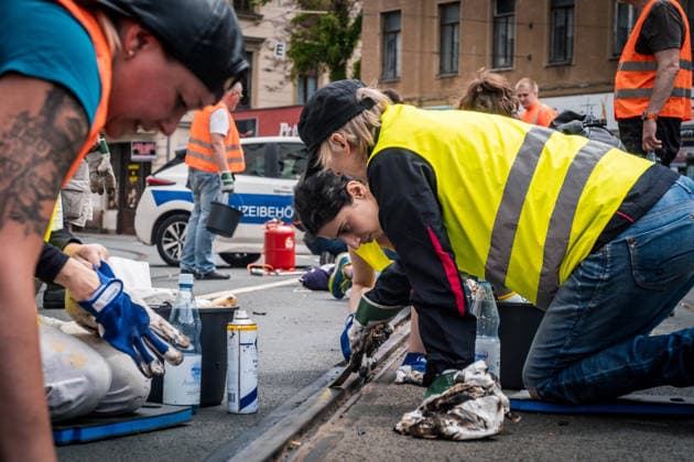 Freiwillige Helfer reinigen gemeinsam mit Mitarbeitenden der Leipziger Verkehrsbetriebe (LVB) Straßenbahngleise an der Leibnizstraße in Leipzig (Sachsen) von geschmolzenem Bitumen. Die Arbeiten sind Teil eines dritten Subbotniks zur Beseitigung der Hitzeschäden am Straßenbahnnetz. Aufnahme vom 4. Juli 2026. Hilfsaktion Leipzig *** Volunteers are working alongside employees of the Leipzig Public Transportation Authority (LVB) to clean melted bitumen from the tram tracks on Leibnizstraße in Leipzig, Saxony. The work is part of a third subbotnik aimed at repairing heat damage to the tram network. Photo taken on July 4, 2026. VolunteerLeipzig Relief Effort