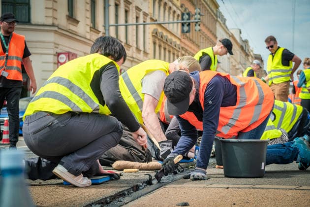 Freiwillige Helfer reinigen gemeinsam mit Mitarbeitenden der Leipziger Verkehrsbetriebe (LVB) Straßenbahngleise an der Leibnizstraße in Leipzig (Sachsen) von geschmolzenem Bitumen. Die Arbeiten sind Teil eines dritten Subbotniks zur Beseitigung der Hitzeschäden am Straßenbahnnetz. Aufnahme vom 4. Juli 2026. Hilfsaktion Leipzig *** Volunteers are working alongside employees of the Leipzig Public Transportation Authority (LVB) to clean melted bitumen from the tram tracks on Leibnizstraße in Leipzig, Saxony. The work is part of a third subbotnik aimed at repairing heat damage to the tram network. Photo taken on July 4, 2026. VolunteerLeipzig Relief Effort