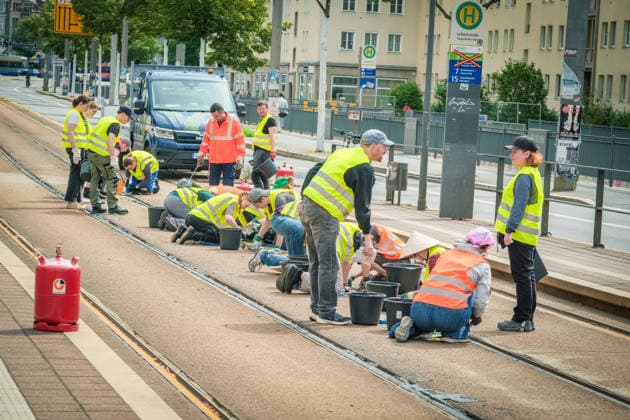 Freiwillige Helfer reinigen gemeinsam mit Mitarbeitenden der Leipziger Verkehrsbetriebe (LVB) Straßenbahngleise an der Leibnizstraße in Leipzig (Sachsen) von geschmolzenem Bitumen. Die Arbeiten sind Teil eines dritten Subbotniks zur Beseitigung der Hitzeschäden am Straßenbahnnetz. Aufnahme vom 4. Juli 2026. Hilfsaktion Leipzig *** Volunteers are working alongside employees of the Leipzig Public Transportation Authority (LVB) to clean melted bitumen from the tram tracks on Leibnizstraße in Leipzig, Saxony. The work is part of a third subbotnik aimed at repairing heat damage to the tram network. Photo taken on July 4, 2026. VolunteerLeipzig Relief Effort
