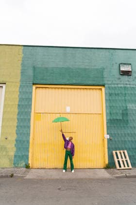Non-binary person holding green umbrella in front of yellow shutter door model released, Symbolfoto, AFVF09355