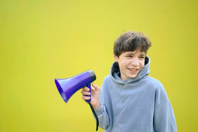 Boy holding a purple megaphone and smiling against a yellow background model released, Symbolfoto, ANAF06018