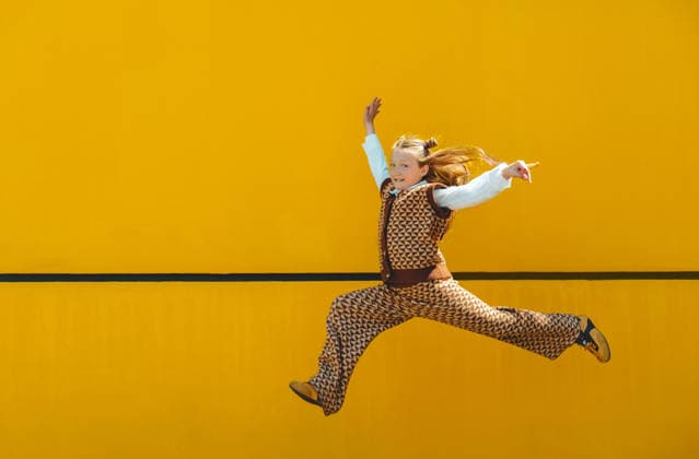 Energetic girl performs a jumping dance against a yellow wall model released, Symbolfoto, AAF00643