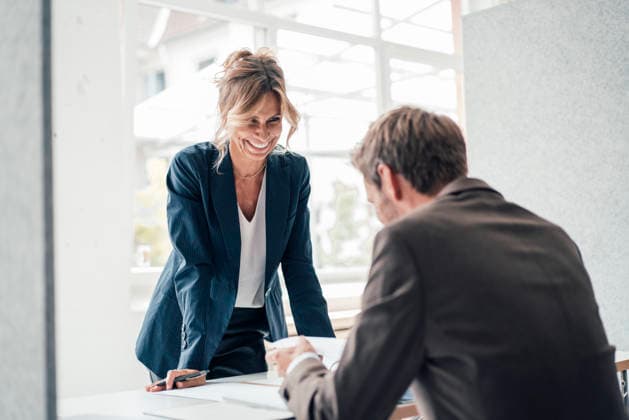 Happy businesswoman leaning on desk looking at client in office model released, Symbolfoto property released, JOSEF14114