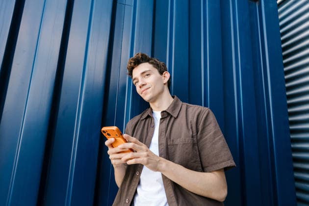 Young man holds smartphone outdoors against blue metal wall model released, Symbolfoto, EGAF02687