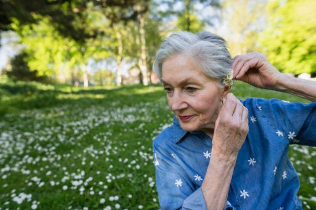 Smiling retiree putting a daisy behind the ear in a sunny park model released, Symbolfoto, KNSF12473