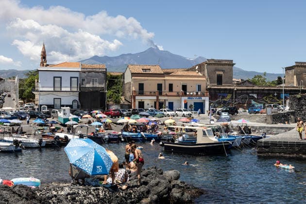 IPA86401869 - Pozzillo, Catania, July 5, 2026: Mount Etna™s eruption as seen from the coast; swimmers are enjoying a dip in the sea at the small harbor, with a cloud of smoke in the background  Copyright: xFrancescoxEnriquezx xFrancescoxEnriquezx 86401869
