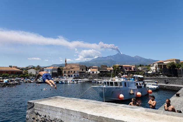 IPA86402107 - Pozzillo, Catania, July 5, 2026: Mount Etna™s eruption as seen from the coast; swimmers are enjoying a dip in the sea at the small harbor, with a cloud of smoke in the background  Copyright: xFrancescoxEnriquezx xFrancescoxEnriquezx 86402107
