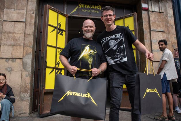Metallica fans by the pop up ship in London, UK - 5Jul 2026 Two fans pose for a photo with their bags front of the Metallica pop up shop in London. Metallica heavy metal band is having two concerts in London over the weekend as part of the M72 World Tour. Hundreds of Metallica fans were seen queuing up to buy some memorabilia by the Metallica pop up shop which is open for 4 days in London, UK. London United Kingdom Copyright: xKrisztianxElekx xSOPAxImagesx SSS_20260705_POPUP_SHOP_0011005017