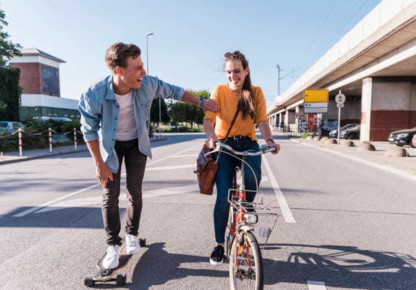 Young man on skateboard holds smiling woman riding bicycle in city model released, Symbolfoto, UUF37215