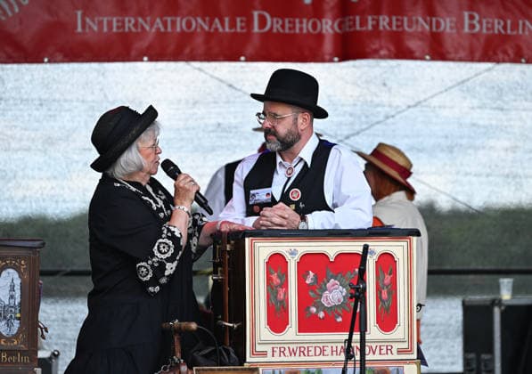 (260706) -- BERLIN, July 6, 2026 -- A host (L) interacts with a barrel organ player in Berlin, Germany, July 5, 2026. The International Barrel Organ Festival 2026 was held in Berlin from July 3 to 5. Barrel organ players from across the world gathered here to entertain residents and visitors with a nostalgic musical celebration. ) GERMANY-BERLIN-BARREL ORGAN FESTIVAL ZhangxHaofu 