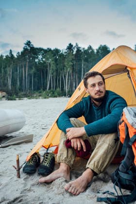 Backpacker sitting in front of his tent on the beach model released, Symbolfoto, VPIF00422