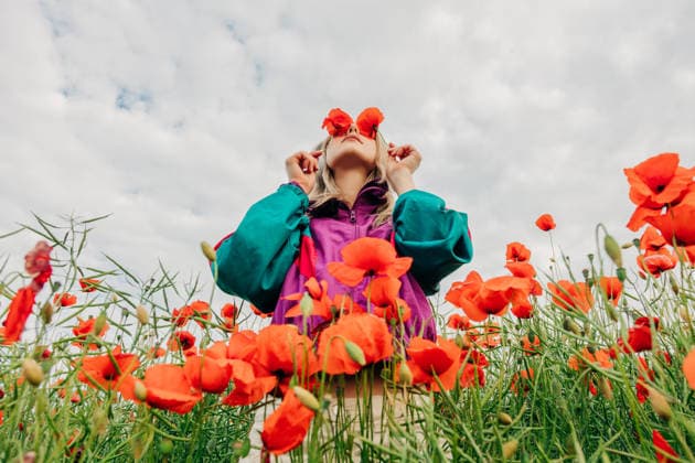 Woman in retro tracksuit covers eyes with red poppies in a meadow model released, Symbolfoto, VSNF05132