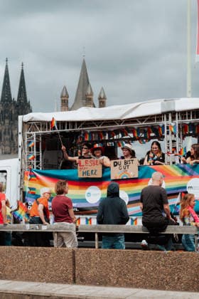 05.07.26, Cologne Pride 2026, parade and demonstration for diversity and equality People ride on a decorated Cologne Pride float in front of Cologne Cathedral and Great St. Martin Church during Cologne Pride 2026. Signs on the float read Lesben gegen Merz (Lesbians against Merz) and Du bist gut genug (You are enough). Cologne Cologne NRW Germany