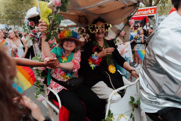 05.07.26, Cologne Pride 2026, parade and demonstration for diversity and equality Two participants ride in a flower-decorated carriage during Cologne Pride 2026, wearing rainbow accessories and interacting with people along the parade route. Cologne Cologne NRW Germany