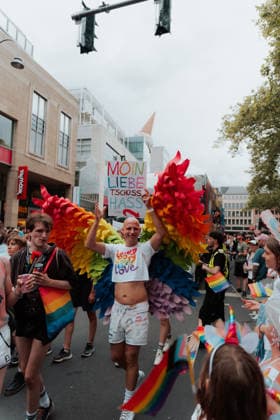 05.07.26, Cologne Pride 2026, parade and demonstration for diversity and equality A Cologne Pride participant with large rainbow wings holds a handmade sign reading Moin Liebe, Tschüss Hass (Hello love, goodbye hate) while walking through the parade. Cologne Cologne NRW Germany