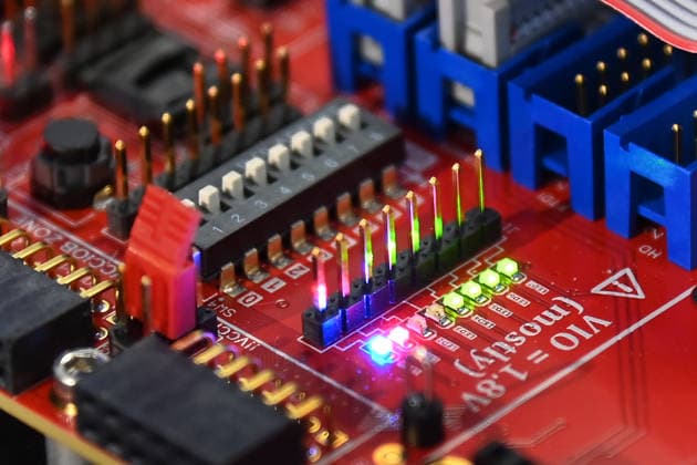 Nahaufnahme einer roten Elektronikplatine mit Steckverbindern, DIP-Schalter, Stiftleisten und Flachbandkabel. 5.Bayerischer Halbleiter-Kongress am 06.07.2026 in Muenchen. *** Close-up of a red circuit board with connectors, DIP switches, pin headers, and ribbon cables 5th Bavarian Semiconductor Congress on July 6, 2026, in Munich