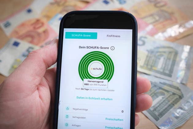 Nahaufnahme einer Hand, die ein Smartphone hält, auf dem über die bonify-App der aktuelle SCHUFA-Score mit der Bewertung HERVORRAGEND (885 von 999 Punkten) angezeigt wird. Im Hintergrund liegen unscharf Euro-Geldscheine. *** A close-up of a hand holding a smartphone, on which the bonify app displays the current SCHUFA score with a rating of EXCELLENT (885 out of 999 points). Euro banknotes are visible in the background, out of focus. Nordrhein-Westfalen Deutschland, Germany GMS202755