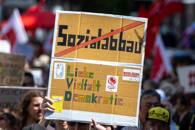 Demonstration für Solidarität statt Sozialabbau, Nürnberg, 11.07.2026 Ein Demonstrant hält ein handgeschriebenes Pappschild mit durchgestrichenem Schriftzug Sozialabbau und den Worten Liebe, Vielfalt, Demokratie in die Höhe. Im Hintergrund sind weitere Teilnehmer und rote Fahnen zu sehen. Das Bündnis UNKÜRZBAR Mittelfranken demonstriert gegen das Reformpaket der Bundesregierung. Nürnberg Bayern Deutschland *** Demonstration for Solidarity Instead of Social Cuts, Nuremberg, July 11, 2026 A demonstrator holds a handwritten cardboard sign with the words Social Cuts crossed out and the words Love, Diversity, Democracy. In the background, other participants and red flags can be seen. The UNKÜRZBAR Middle Franconia Alliance is dem 20260711-1V9A5349-M4000