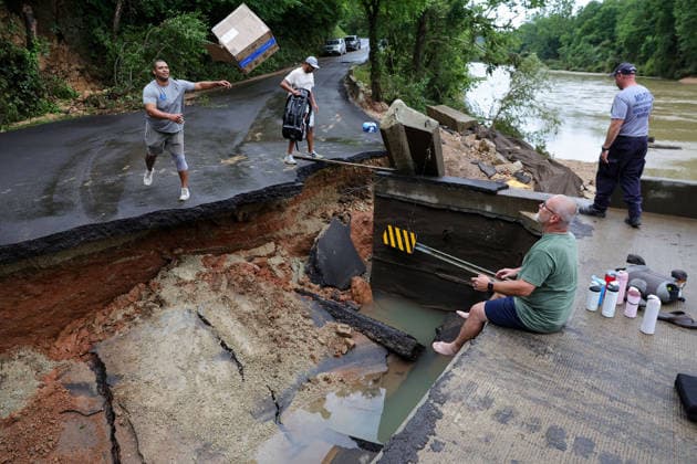 July 11, 2026, Lesterville, Mo, USA: Trey Millard, left, of Columbia, Missouri, throws a box to his dad, Rob Millard, right, across a broken County Road 364 as his brother, Ky Millard, prepares to hand off a baby carrier in Lesterville, Missouri, on Saturday, July 11, 2026. Flash flooding from the nearby Black River submerged the nearby campgrounds and eroded the road, stranding the Millards who spent the last week camping and was planning to leave the day the flooding came. There s people who lost a lot more, Trey Millard said. Lesterville USA  - ZUMAm67_ 20260711_zaf_m67_003 Copyright: xLizxRymarevx