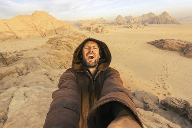 Fröhlicher, glücklicher, aufgeregter abenteuerlustiger Reisender posiert im Beduinen Abaya Umhang und macht ein Wüsten Selfie aus einem hohen Winkel auf einer Klippe in der Wüste Wadi Rum im Freien. Verrücktes Reise Konzept Joyful happy excited adventurous traveler pose Wearing Bedouin Abaya Cloak Taking High Angle Desert Selfie on cliff in Wadi Rum desert outdoors. Crazy traveler concept Copyright: imageBROKER EvaldasxMikoliunas ibxemi18369155.jpg ,model released, Symbolfoto ,property released