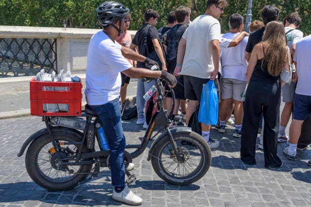 July 11, 2026, Rome, Italy: A worker replacing eBike batteries waits for some tourists to finish taking a group photo before continuing his journey during the hottest hours of the day when Italy is trapped in the grip of the July heat in Rome. After the storms of the past few days, a new wave of intense heat is expected across Italy. The subtropical anticyclone will once again dominate the Italian weather landscape, paving the way for a new phase of intense heat destined to affect much of the country for the entire next week. Rome Italy  - ZUMAv147 20260711_zip_v147_003 Copyright: xMarcelloxValerix