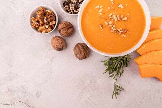 Kürbissuppe mit Walnüssen in einer weißen Schüssel, garniert mit Kürbisscheiben und Gewürzen ? Draufsicht auf weißem Marmorhintergrund mit Freiraum für Text Pumpkin soup with walnuts in white bowl decorated with pumpkin slices and spices top view flat lay with copy space (License=RF) Copyright: xZoonar.com IlonaxShorokhovax 25277366