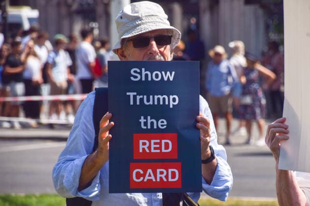 July 13, 2026, London, England, United Kingdom: An activist holds a Show Trump the red card placard during a protest in Parliament Square against the US-UK drug deal. An analysis has suggested that the trade deal could lead to 229,000 excess deaths in England as a result of diverting billions of pounds from essential NHS services to pay for new medicines. London United Kingdom  - ZUMAv130 20260713_zip_v130_012 Copyright: xVukxValcicx