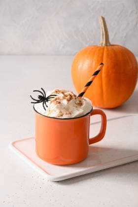 Halloween-Kürbis-Latte mit Schlagsahne und Spinnen als Garnitur Pumpkin latte coffee with whipped cream decorated spiders in orange mug on white kitchen background. Vertical format. Funny food for child in Halloween party. (License=RF) Copyright: xZoonar.com SvetlanaxLazhkox 25303864