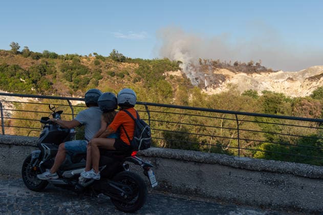 Wildfire erupts near Campi Flegrei volcanic area in Italy POZZUOLI, ITALY - JULY 13: People look a helicopter as it drops water over a wildfire in the Solfatara volcanic crater in the Campi Flegrei (Phlegraean Fields) volcanic region in Pozzuoli on July 13, 2026. The fire broke out in the undergrowth and quickly spread in the Pisciarelli area to several car dealerships, causing fuel tanks and tyres to explode. Eliano Imperato Anadolu Pozzuoli Italy. Editorial use only. Please get in touch for any other usage.  Copyright: x2026xAnadoluxElianoxImperatox