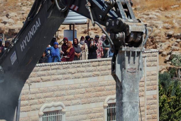 Hebron West Bank Home Demolition Palestinian residents watch as an excavator operates during a home demolition in Al-Deirat, south of Hebron, occupied West Bank on July 14, 2026. Israeli forces demolish the home of Osama Masaaf on the grounds that it lacked an Israeli-issued building permit, displacing a Palestinian family of eight. Hebron West Bank Palestinian Territories Copyright: xMosabxShawerx