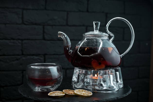 Schwarzer aromatischer Kräutertee mit Minzblättern und Ingwer sowie Orangen- und Fruchtscheiben in einer antiken Glasteekanne neben einer Glastasse auf einem Holztisch in einem CafÃ . Schönes Teeservice. Ein Teeset. *** Schwarzer Aromatic Herbal tea with Minzblättern and Ginger and Oranges and Fruit slices in a antique Glass teapot next to a Glass cup at a Wooden table in a cafÃ Beautiful Tea service a Tea 1102838702