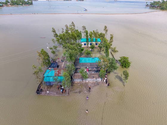 Aftermath Of Floodwaters In Chattogram A high-angle drone shot shows local residents wading through knee-to-waist-deep floodwaters outside an isolated homestead in Banshkhali, Chattogram, Bangladesh, on July 14, 2026. Flood waters in Banshkhali and Satkania in Chittagong are slowly receding, revealing collapsed mud houses, damaged structures, destroyed brick kilns and severely damaged agricultural land. The flooding has displaced thousands of people. Chattogram Bangladesh  Copyright: xZakirxHossainx originalFilename: hossain-notitle260714_npU8U.jpg